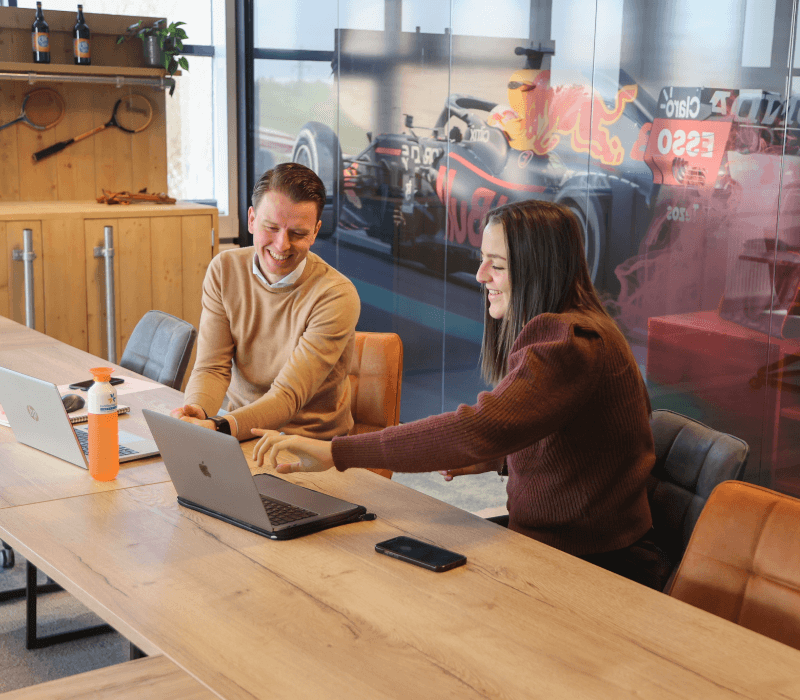 Twee medewerkers van CertificeringsAdvies Nederland werken samen op een MacBook